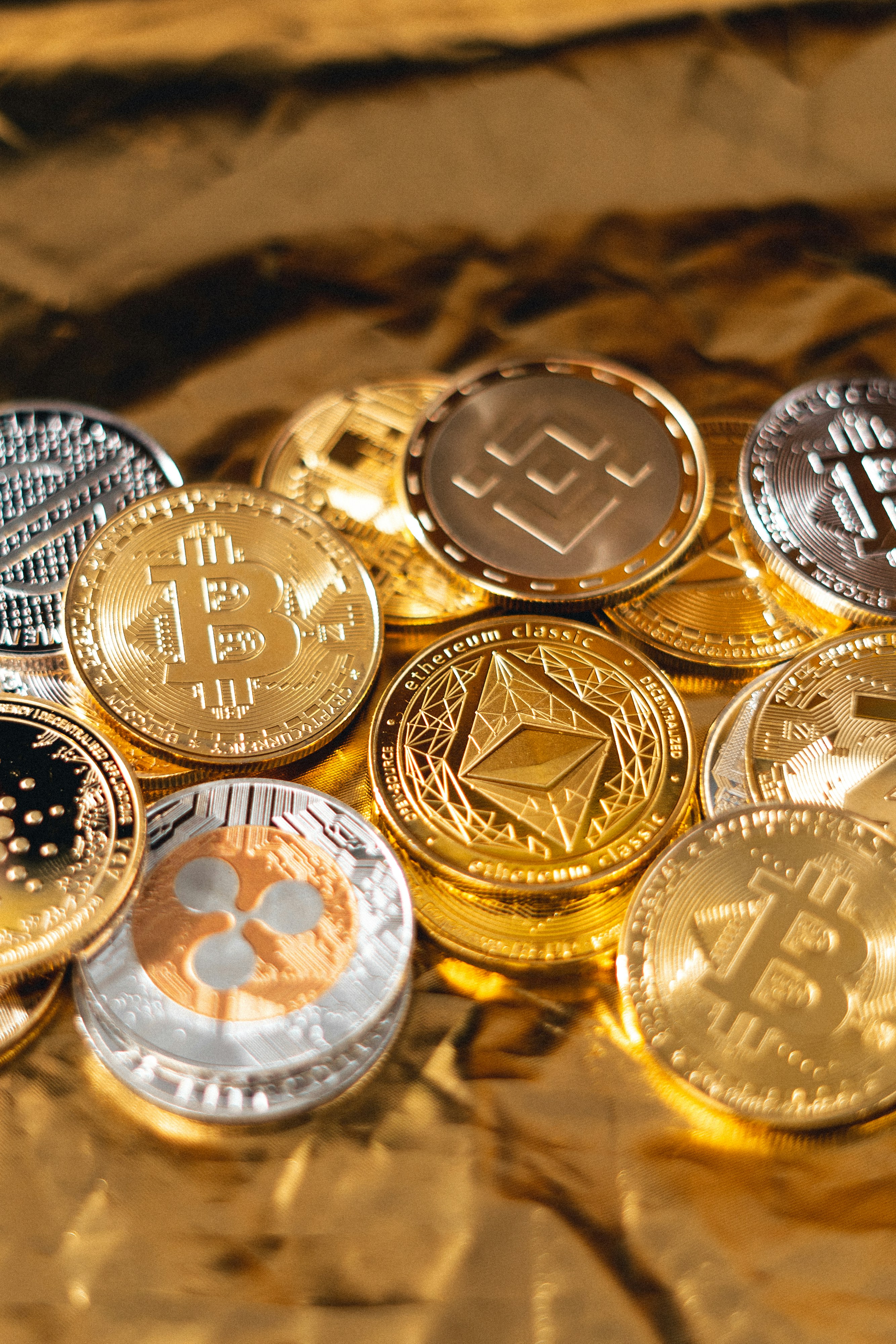 A pile of physical cryptocurrency coins, with gold-colored Bitcoin and Ethereum Classic coins featured prominently in the foreground.