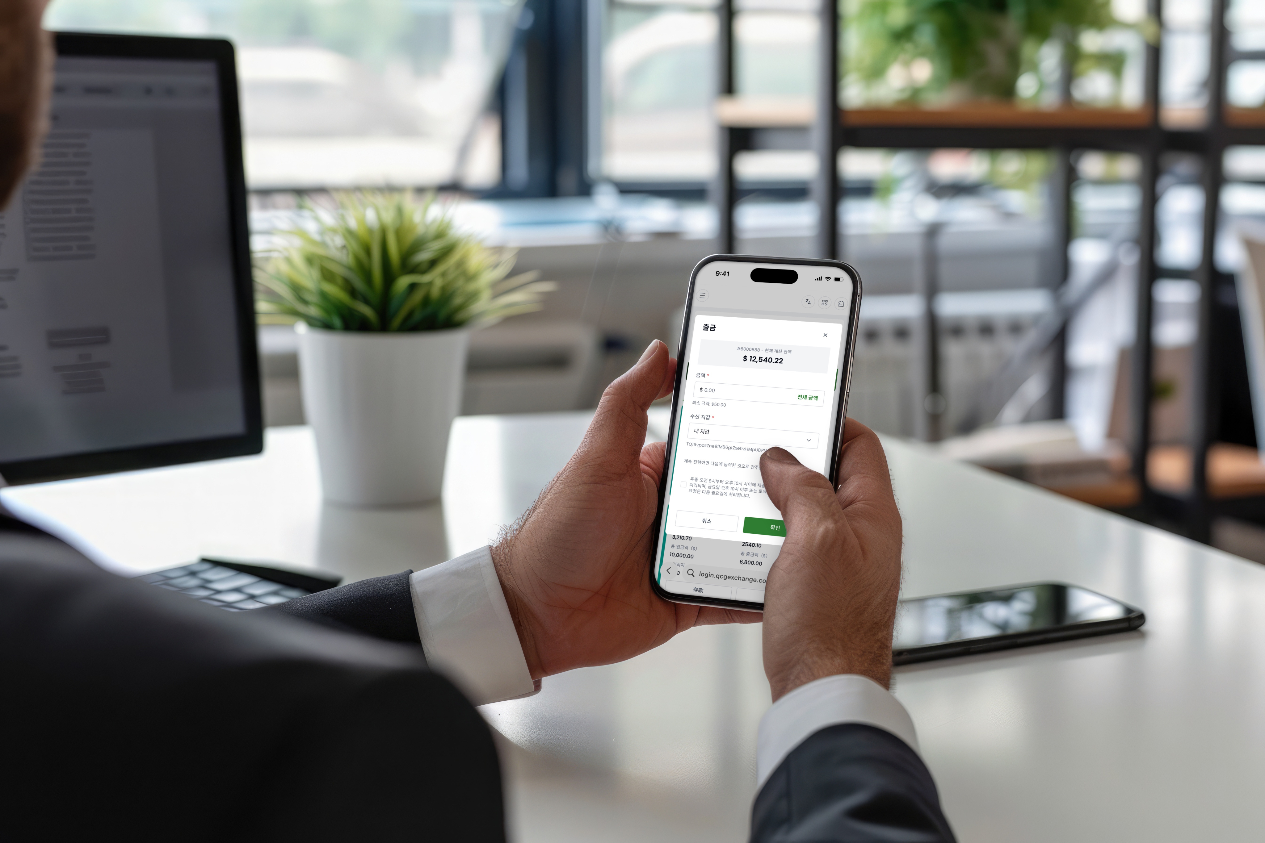 A person's hands holding a smartphone displaying a withdrawal request screen for a trading account in a bright office setting.